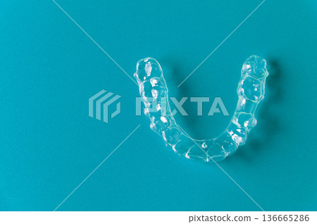 Clear dental aligner placed on a turquoise background, showcasing its transparent design and unique shape for orthodontic treatment and teeth straightening purposes 136665286