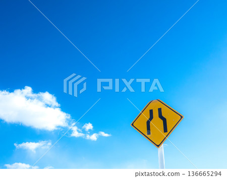 A landscape with blue sky, clouds, and a road sign saying "The road ahead is narrow." 136665294