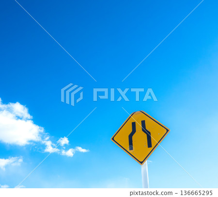 A landscape with blue sky, clouds, and a road sign saying "The road ahead is narrow." 136665295