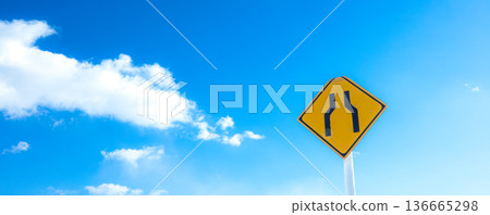 A landscape with blue sky, clouds, and a road sign saying "The road ahead is narrow." 136665298