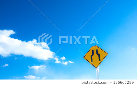 A landscape with blue sky, clouds, and a road sign saying "The road ahead is narrow." 136665299