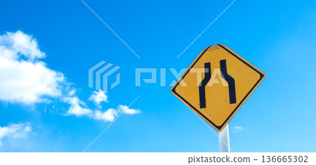 A landscape with blue sky, clouds, and a road sign saying "The road ahead is narrow." 136665302