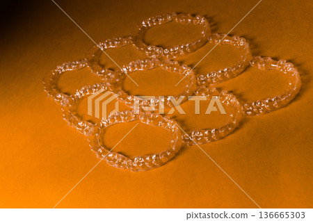 Transparent dental aligners arranged in a circular pattern on a vibrant orange background, showcasing their clear design and smooth edges for orthodontic treatment 136665303