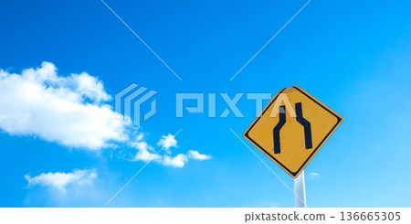 A landscape with blue sky, clouds, and a road sign saying "The road ahead is narrow." 136665305