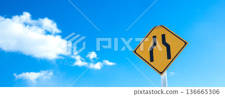 A landscape with blue sky, clouds, and a road sign saying "The road ahead is narrow." 136665306