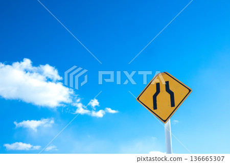 A landscape with blue sky, clouds, and a road sign saying "The road ahead is narrow." 136665307