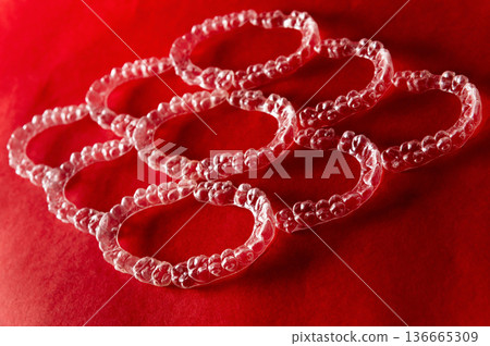 Transparent plastic bracelets arranged in a circular pattern on a vibrant red background, showcasing their unique design and texture with a glossy finish 136665309
