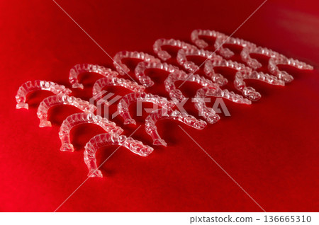 Clear plastic dental aligners arranged in a neat row on a vibrant red background, showcasing their transparent design and unique shape for orthodontic treatment 136665310