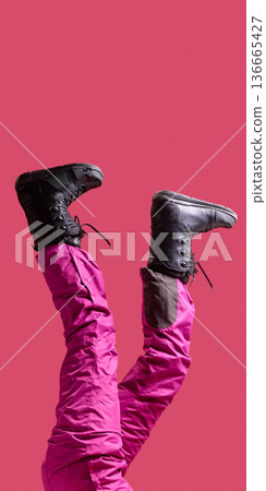Female legs in black snow boots and pink ski pants raised on pink background. Female legs in black snow boots and pink ski pants raised on pink background. 136665427