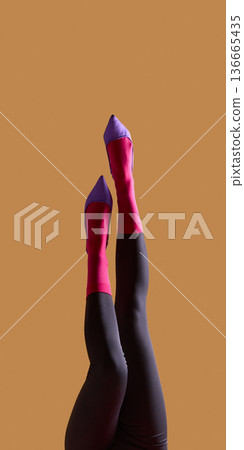 Female legs in pink socks and purple heels raised on beige background. Female legs in pink socks and purple heels raised on beige background. 136665435