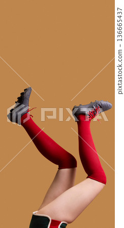 Female legs in red knee socks and black cleats raised on beige background. 136665437