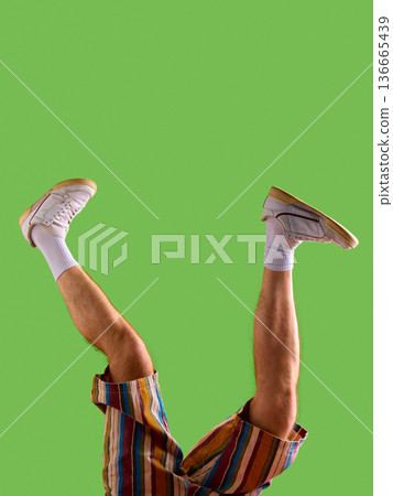 Male legs in white sneakers and striped shorts raised against green background Male legs in white sneakers and striped shorts raised against green background 136665439