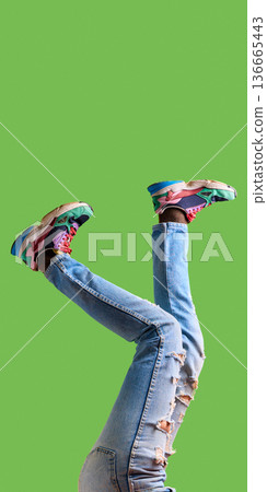 Sideways legs in ripped jeans and colorful sneakers on green background with copy space. 136665443