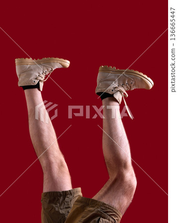 Male legs in beige boots and shorts on red background with copy space. 136665447