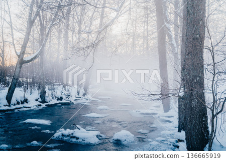 Misty winter forest river with snow and ice at dawn, tranquil Nordic nature scene Misty winter forest river with snow and ice at dawn, tranquil Nordic nature scene 136665919