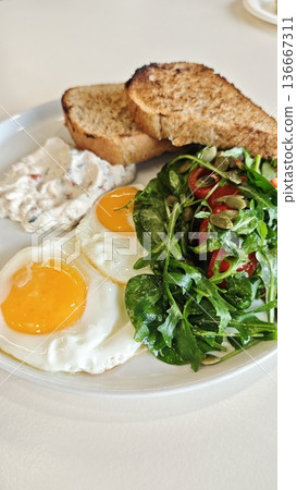 Healthy breakfast with fried egg, toast, vegetable salad and cream spread on white plate. Morning meal concept symbolizing nutrition, balance and fresh lifestyle Healthy breakfast with fried egg, toast, vegetable salad and cream spread on white plate. Morning meal concept symbolizing nutrition, balance and fresh lifestyle 136667311