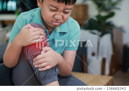 Asian boy showing painful face expression holding red inflamed knee from joint injury or accident. Pediatric healthcare concept of childhood bone problems, growth pain, and orthopedic treatment. Asian boy showing painful face expression holding red inflamed knee from joint injury or accident. Pediatric healthcare concept of childhood bone problems, growth pain, and orthopedic treatment. 136668343