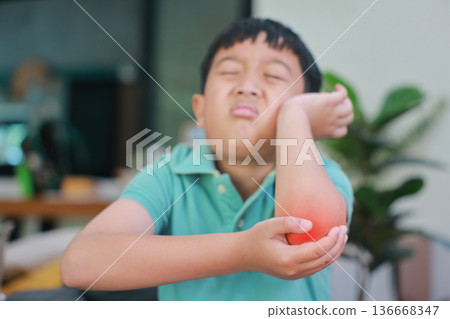 Asian boy suffering from elbow pain with red highlight on painful area, child having arm muscle injury, joint inflammation, accidental bone fracture or skin irritation problem at home. Asian boy suffering from elbow pain with red highlight on painful area, child having arm muscle injury, joint inflammation, accidental bone fracture or skin irritation problem at home. 136668347