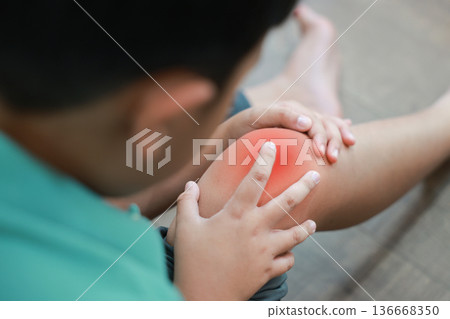 Asian boy showing painful face expression holding red inflamed knee from joint injury or accident. Pediatric healthcare concept of childhood bone problems, growth pain, and orthopedic treatment. Asian boy showing painful face expression holding red inflamed knee from joint injury or accident. Pediatric healthcare concept of childhood bone problems, growth pain, and orthopedic treatment. 136668350