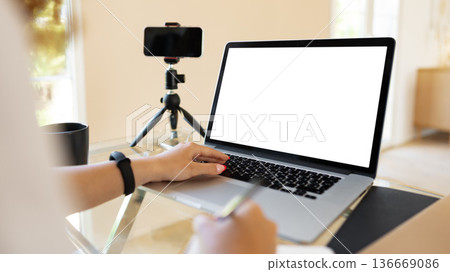 Person using laptop and writing notes with camera setup in modern workspace 136669086