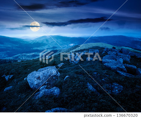mountain landscape in summer with rocks at night. grass under dark sky in full moon light. alpine meadow and rolling hills with boulders. backdrop for evil fiction art or mystery concepts 136670320