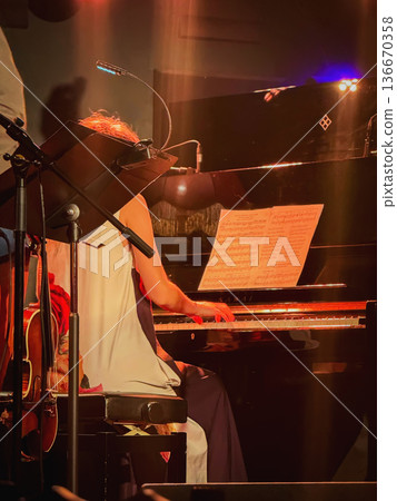 Pianist performing on grand piano with sheet music and microphone on stage during concert with warm lighting. Concept of live music performance, piano recital, classical music event, stage background 136670358