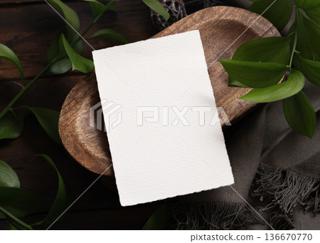 Vertical card on brown wooden tray near green leaves and grey fabric closeup, boho mockup Vertical card on brown wooden tray near green leaves and grey fabric closeup, boho mockup 136670770
