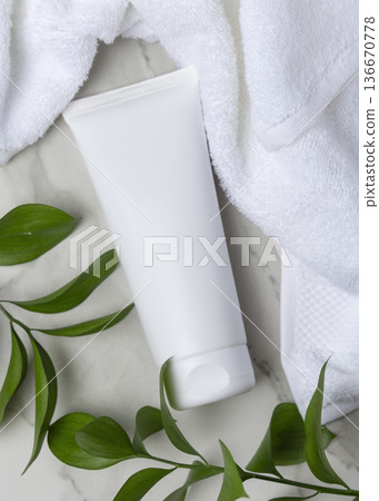 Mockup of blank white cream tube near white bath towel and green leaves. Unbranded cosmetic Mockup of blank white cream tube near white bath towel and green leaves. Unbranded cosmetic 136670778