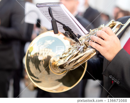 Close up of musician hand playing a golden french horn during outdoor street parade Close up of musician hand playing a golden french horn during outdoor street parade 136671088