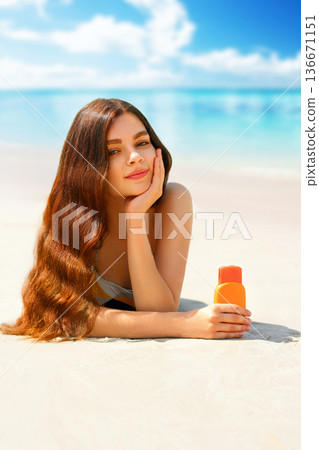 Portrait of gorgeous young woman smiling while relaxing on beach and holding sunscreen bottle Portrait of gorgeous young woman smiling while relaxing on beach and holding sunscreen bottle 136671151