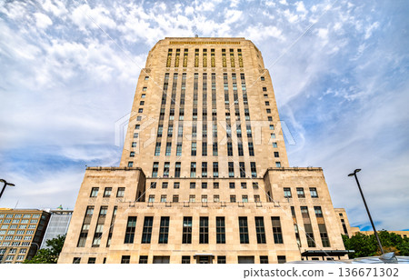 Kansas City City Hall in Missouri. Historic Art Deco government building features a tall limestone facade and vertical windows under a blue sky with clouds Kansas City City Hall in Missouri. Historic Art Deco government building features a tall limestone facade and vertical windows under a blue sky with clouds 136671302