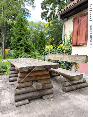 Rustic wooden garden table and bench made of logs against a backdrop of lush greenery Rustic wooden garden table and bench made of logs against a backdrop of lush greenery 136671475