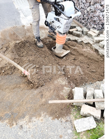 A worker compacts the soil with a vibrating plate 136671478