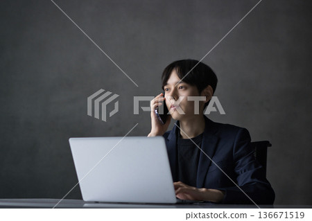 A young businessman talking on a smartphone while looking at a computer A young businessman talking on a smartphone while looking at a computer 136671519