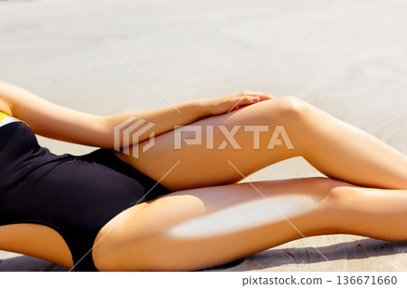 Closeup of beautiful woman applying suntan lotion on leg at beach 136671660