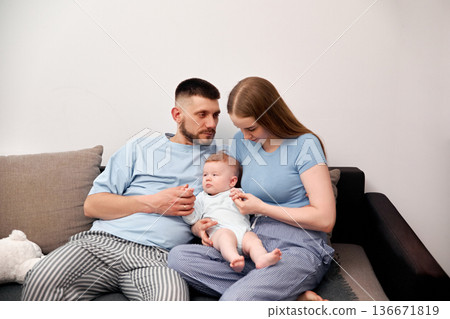 Parents sit on a couch with their baby during a quiet moment at home in the afternoon while sharing a loving experience together Parents sit on a couch with their baby during a quiet moment at home in the afternoon while sharing a loving experience together 136671819