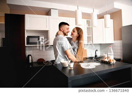 Couple shares a moment in their kitchen as they embrace while preparing breakfast together on a weekend morning at home Couple shares a moment in their kitchen as they embrace while preparing breakfast together on a weekend morning at home 136671840