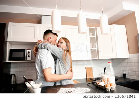 Couple shares a moment in the kitchen while preparing breakfast together in a cozy apartment during morning hours Couple shares a moment in the kitchen while preparing breakfast together in a cozy apartment during morning hours 136671841