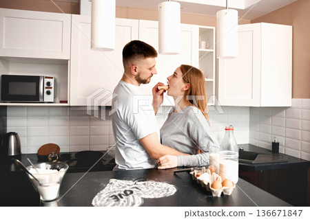 Couple enjoys cooking together in the kitchen while sharing a light moment with food during a sunny afternoon Couple enjoys cooking together in the kitchen while sharing a light moment with food during a sunny afternoon 136671847