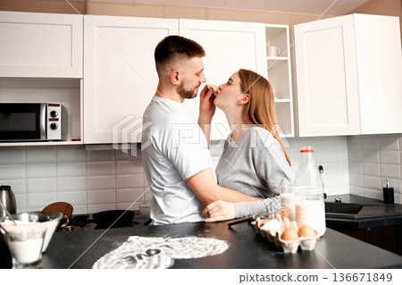 Couple enjoys playful moment in a kitchen while preparing food together on a weekend morning in a modern home setting Couple enjoys playful moment in a kitchen while preparing food together on a weekend morning in a modern home setting 136671849