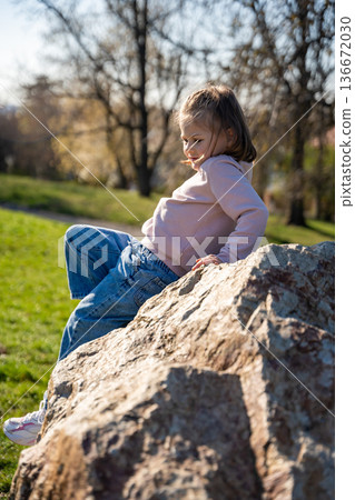 Little girl jumping on decorative stones in city park. Active spring play and outdoor childhood lifestyle. 136672030