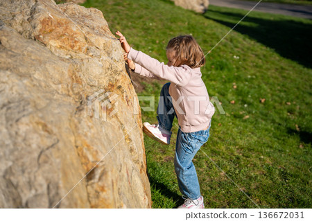 Little girl jumping on decorative stones in city park. Active spring play and outdoor childhood lifestyle. 136672031