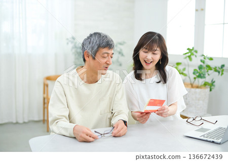 A couple in their 60s looking at their savings passbook in the living room 136672439