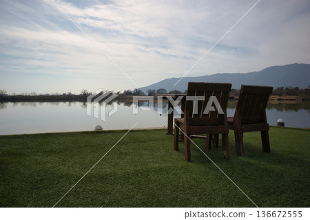 Wooden tables and chairs set up by a scenic lake 136672555