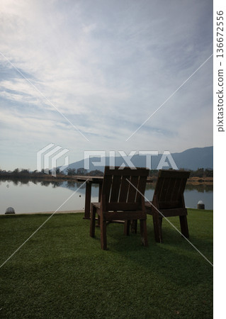 Wooden tables and chairs set up by a scenic lake 136672556