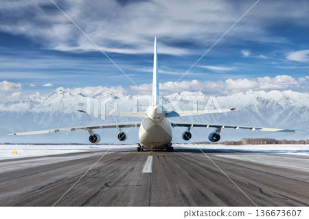 Rear view of big heavy transport airplane on the runway of winter airport on the background of high snow capped mountains Rear view of big heavy transport airplane on the runway of winter airport on the background of high snow capped mountains 136673607