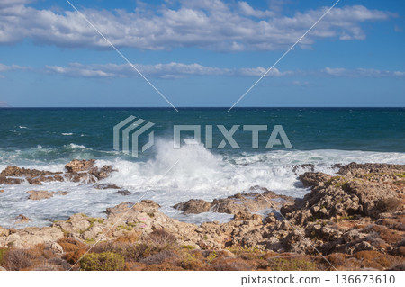 Sea foam crashing against rocky shore. 136673610