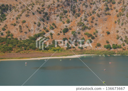Drying mountain lake with wide strip of dried shore and orange rocky slope. Drying mountain lake with wide strip of dried shore and orange rocky slope. 136673667