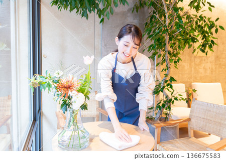 A young female waitress wiping the tables at a cafe A young female waitress wiping the tables at a cafe 136675583