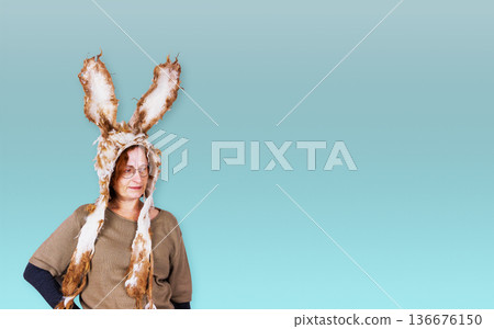 Sstudio portrait of a middle aged woman wearing handmade felted bunny hat with long ears standing against blue background. Copy space 136676150